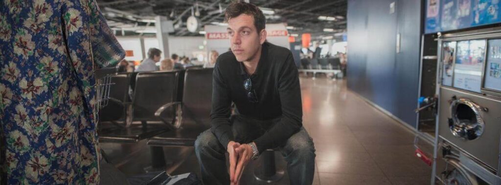 Pessoa sentada em um banco de aeroporto com a mão na cabeça, em expressão de cansaço e frustração, representando o dano moral sofrido.