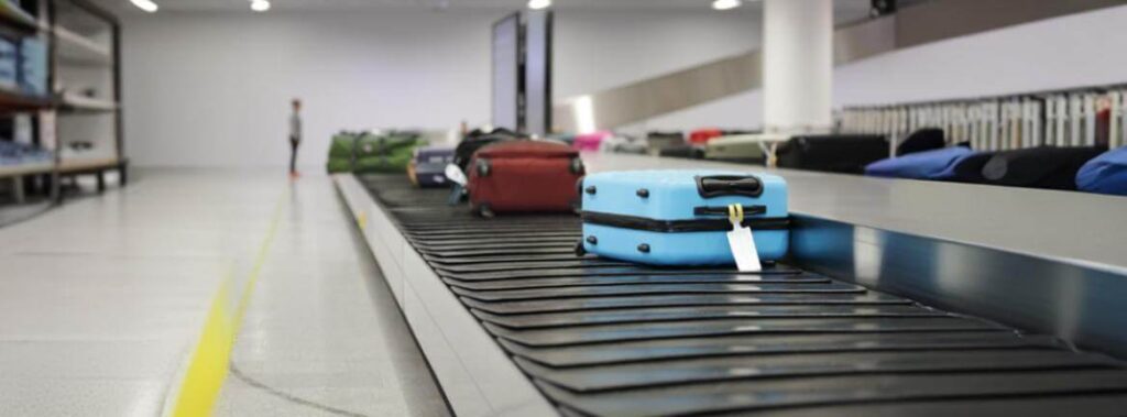 Passageiro olha preocupado para uma esteira de restituição de bagagens vazia em um saguão de aeroporto.