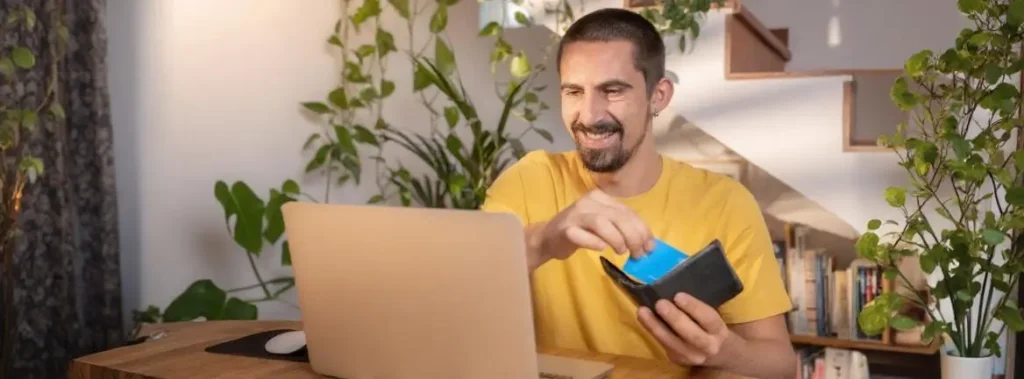 Homem sorri ao conferir seu notebook e conferir a restituição dos valores perdidos na fraude bancária.